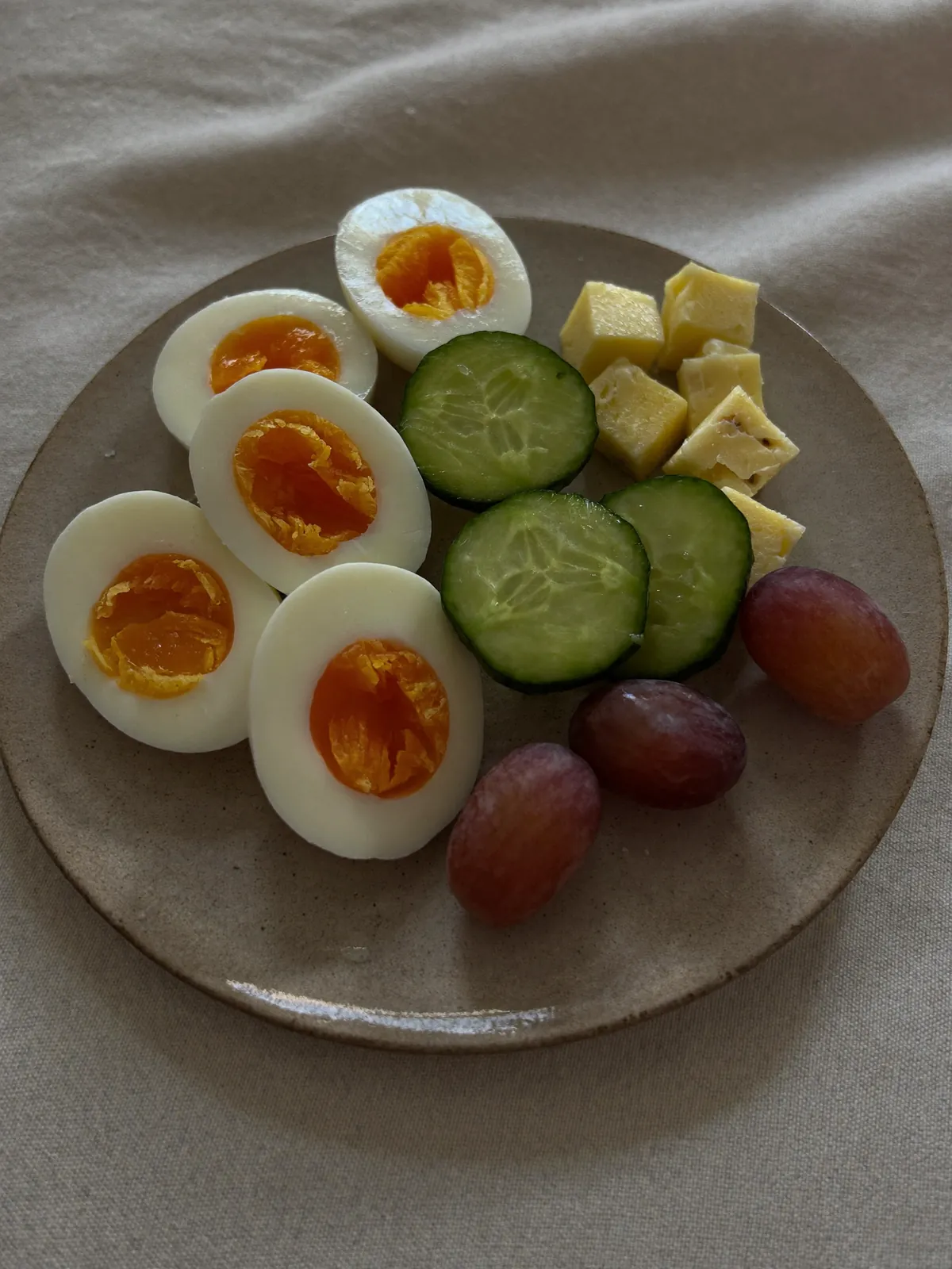 A cold snack plate of halved hard boiled eggs, cucumber rounds, cheese cubes and grapes.