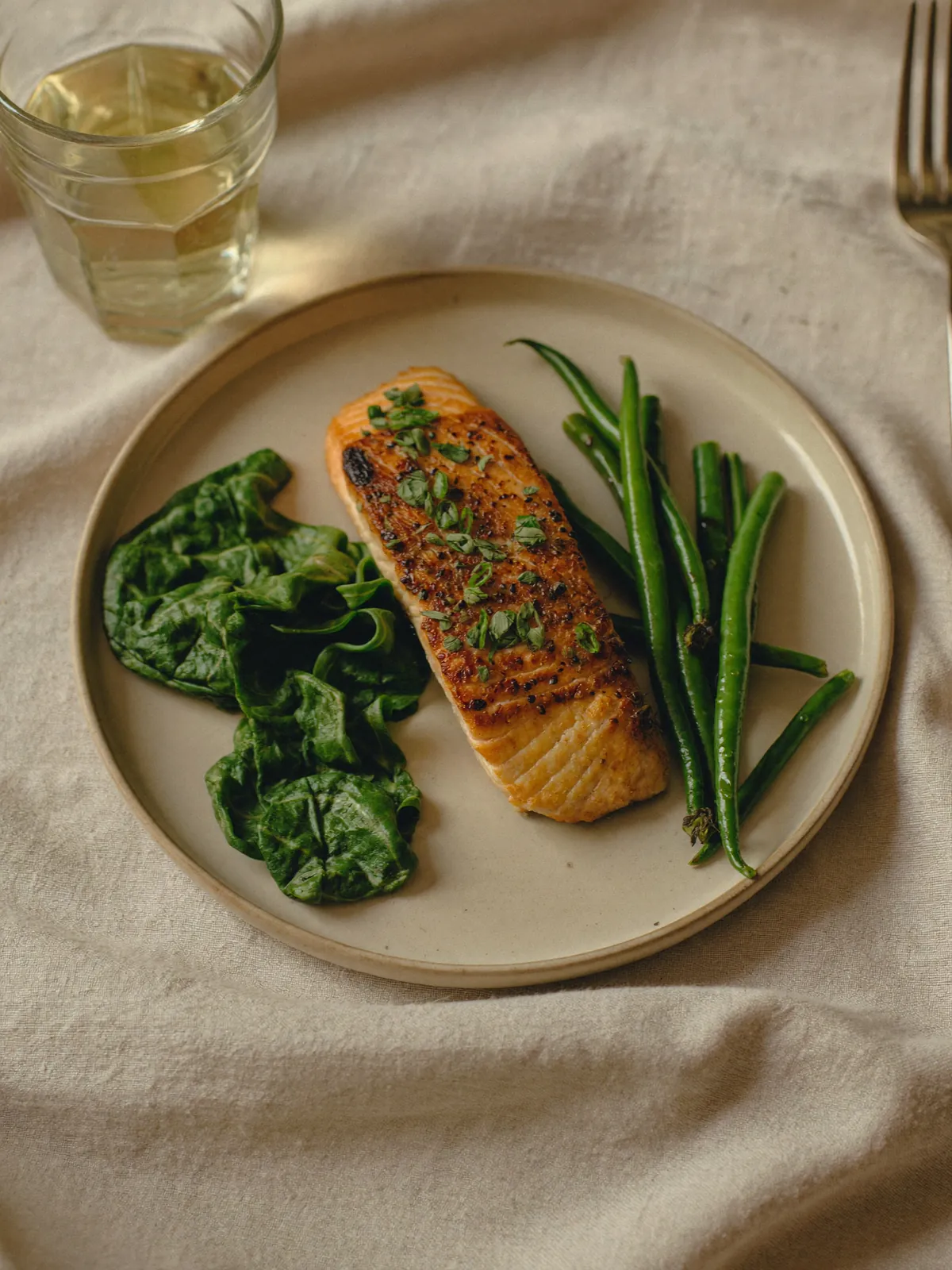 A small plate of seared salmon with wilted spinach and green beans, a glass of water beside it.